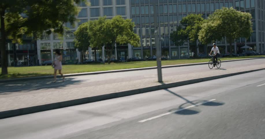 A man rides his bike down a city street past an office building as other people walk along
