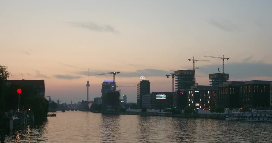 A waterfront of a river with buildings cranes and lights at dusk