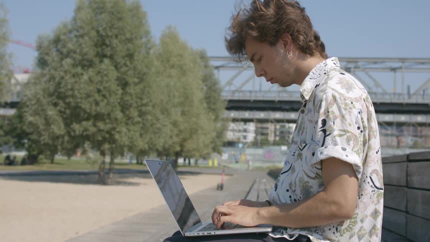 A man sitting in a park working on a laptop
