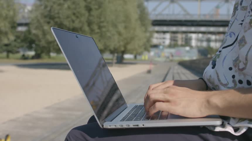 A person typing on a laptop in a park