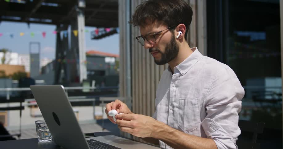 Man working on a laptop outdoors puts on earbuds