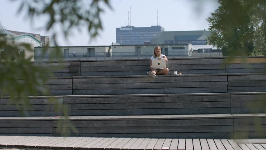 A teenage girl sitting outside her school opens her laptop up