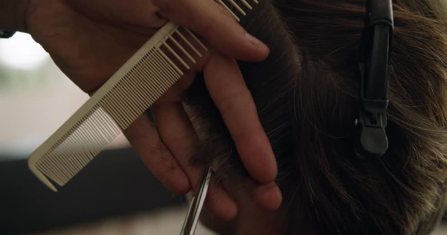A person cuts the hair of a a person sitting in a chair indoors