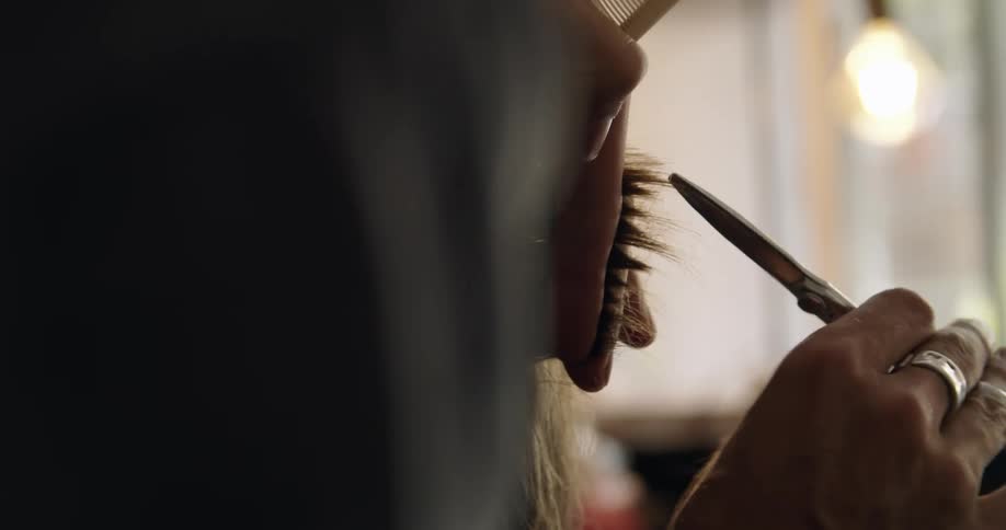 A hairdresser is cutting blonde hair short