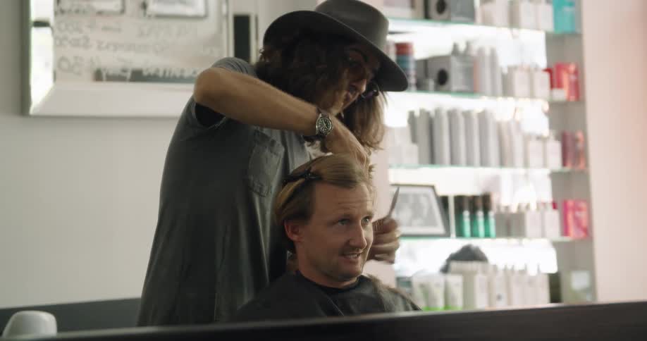 A man with a hat and glasses cutting another mans hair