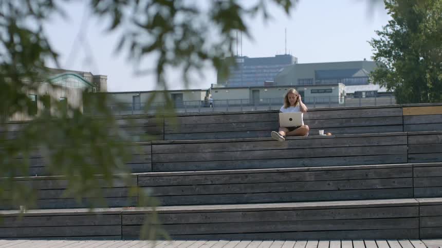 A teenage girl sits outside her school and uses her laptop