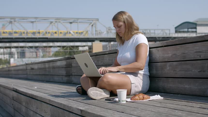 A woman sitting on a bench working on a laptop