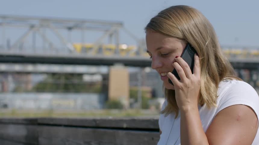 A teenage girl outside answers her cell phone and talks as a train goes past