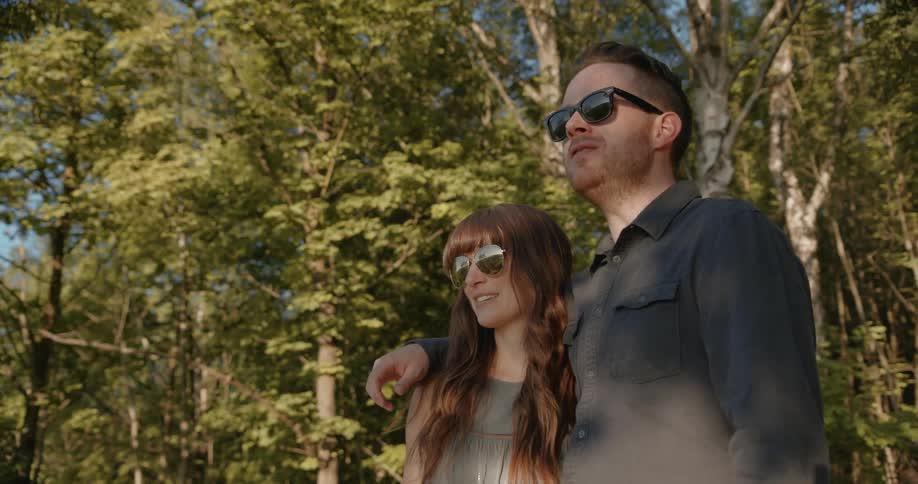A man and woman in sunglasses talk in a forest
