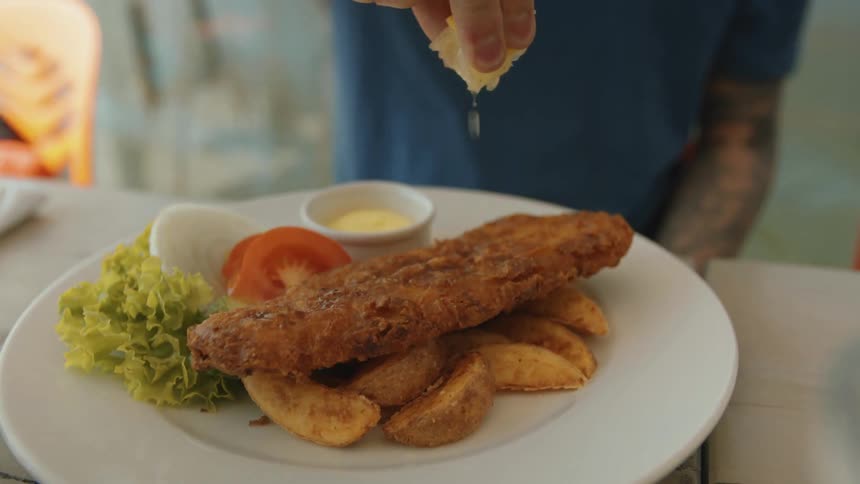 A person squeezes lemon juice over a piece of fried fish
