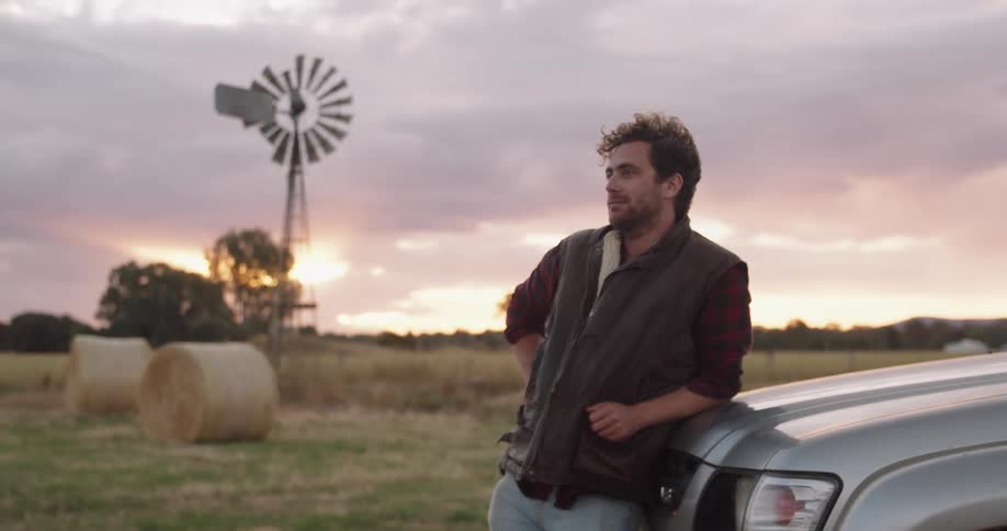 A man leans on his vehicle parked in a large rural farmland
