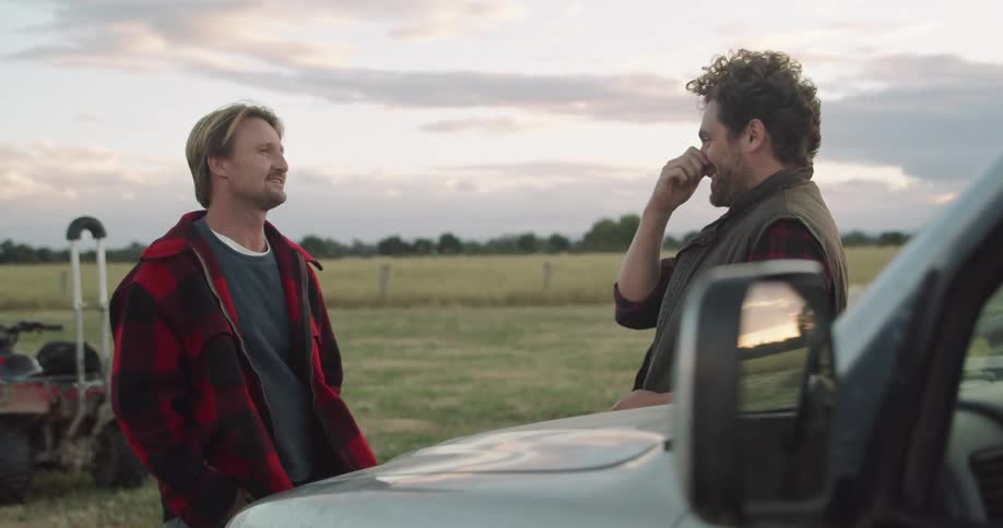Two men are talking outdoors by a car