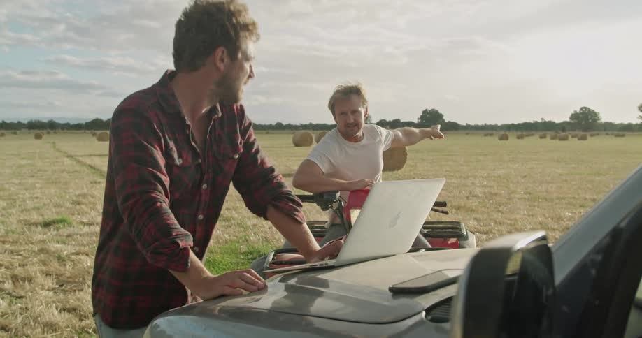 Two men talk and point towards the farm land