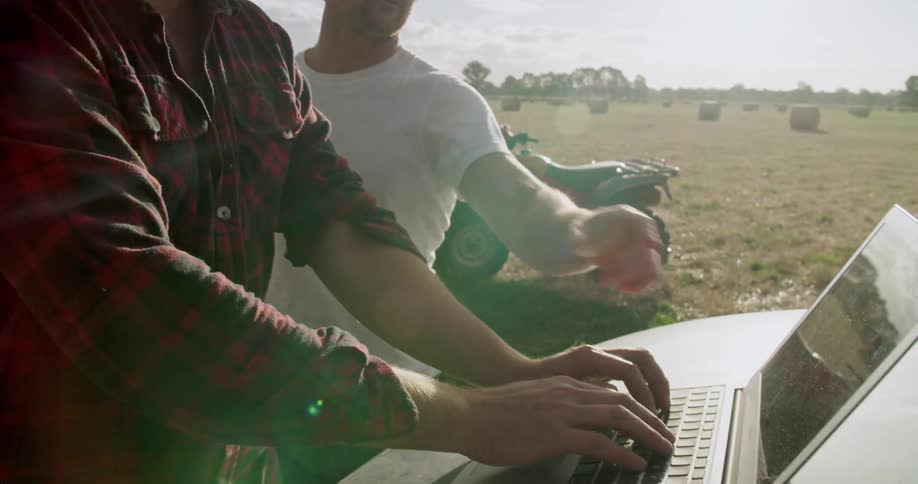 Two men chat on an open farm field and turn to a laptop to use