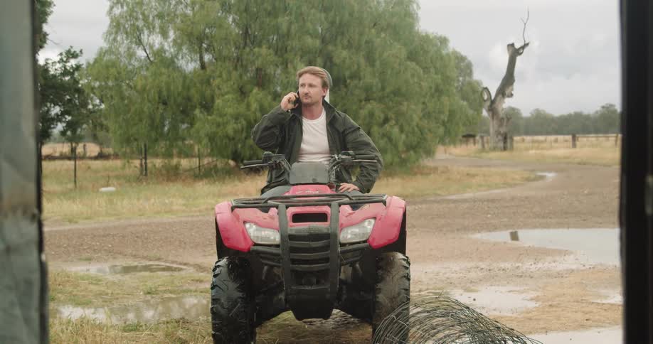 Man sits on four wheeler while talking on mobile phone