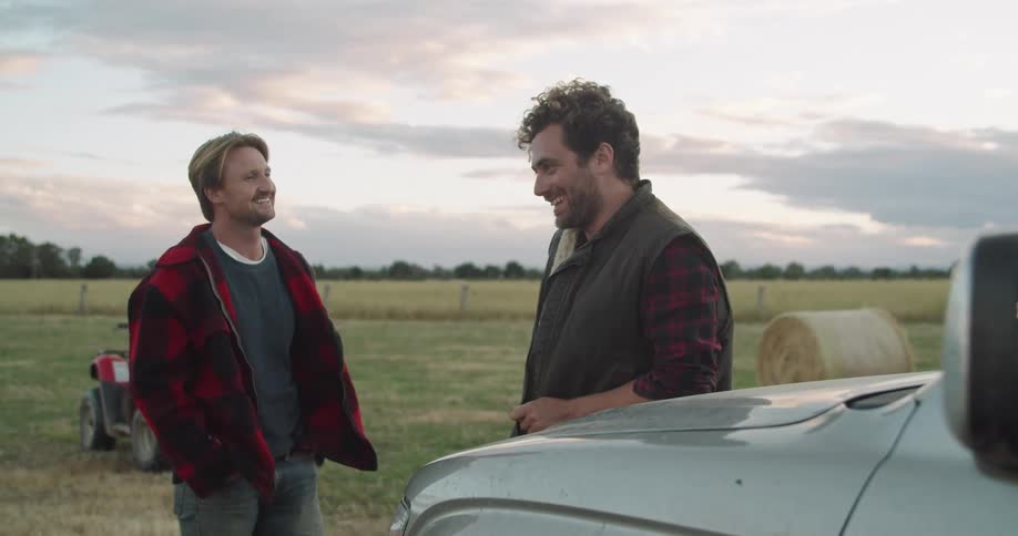 Two men standing outside next to a field in farmland talking and laughing with each other