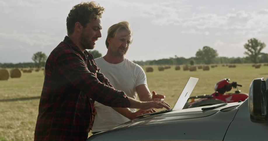 Two men are standing outdoors by a car in spring