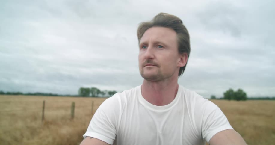 A man wearing a white t shirt rides on an atv on a field on a sunny day