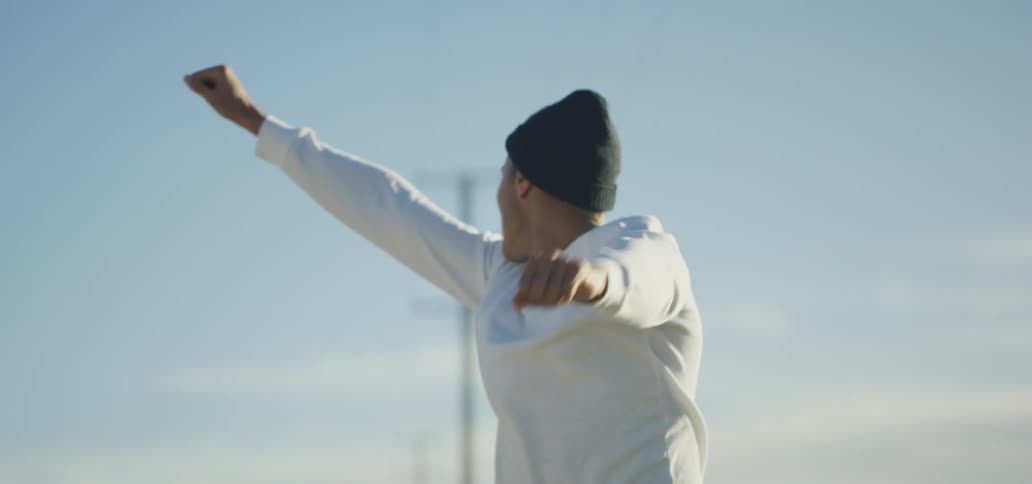 A man raises his arms in celebration as he jumps up and down while looking around at his surroundings outdoors during the day