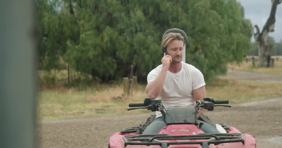 A man talks on a phone while sitting on an atv outdoors