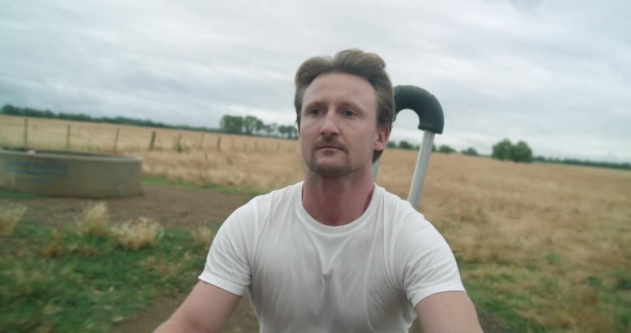 Under a cloudy sky a man drives his atv along a large grassy field