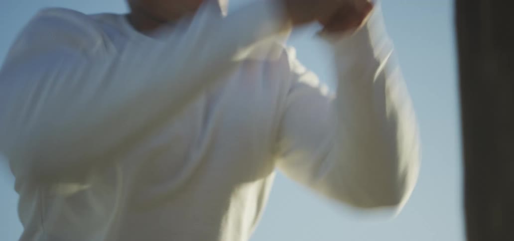 A young man throws punches at a wooden pole outdoors on a sunny day