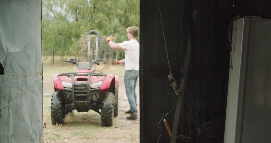A man carries barbed wire from a shed to an atv