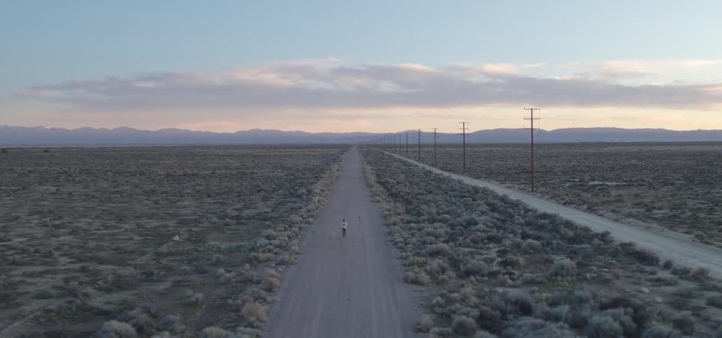 An aerial view of a man walking along a remote road at dusk