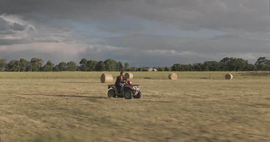 A man rides an all terrain vehicle through a wide open field on a farm