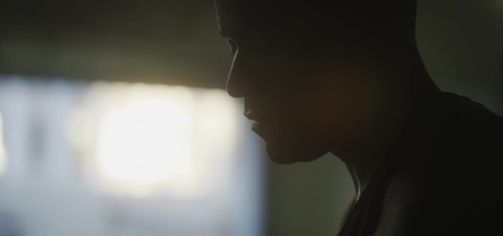 A man stands in profile inside a dark room next to a window