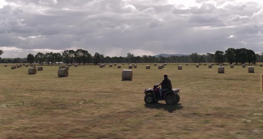 Man rides atv through field past hale bales with mountains on horizon
