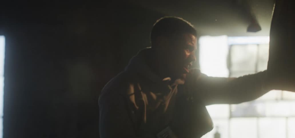Man indoors wearing boxing gloves punching the air in front of a window with a flare of sunlight