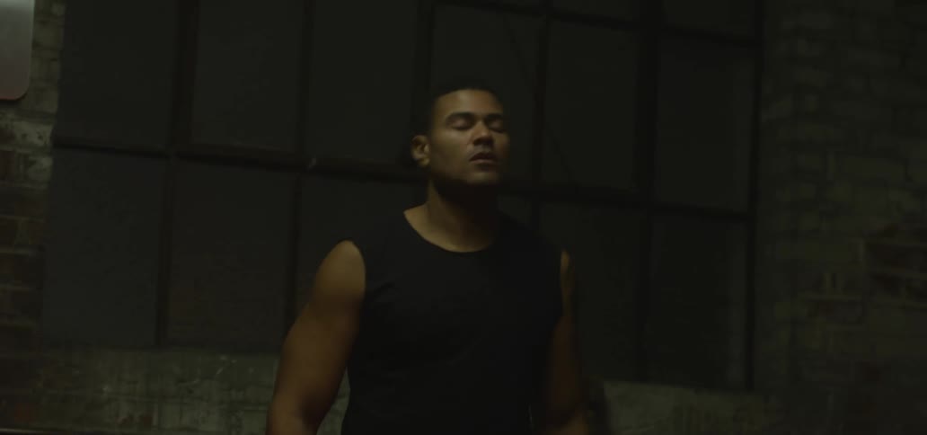 A muscular man with his fists wrapped for boxing stretches his neck while warming up