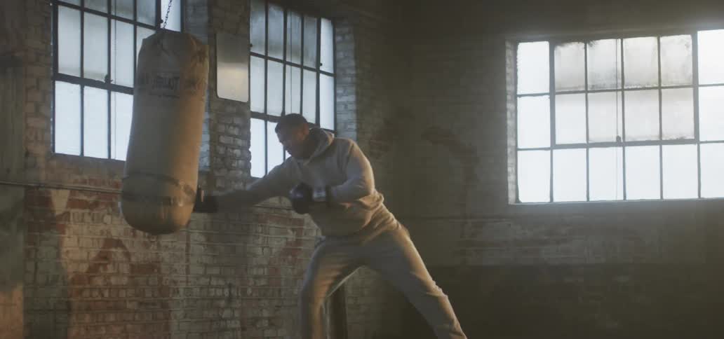Strong young man boxing training inside an abandoned warehouse with a punching bag at morning