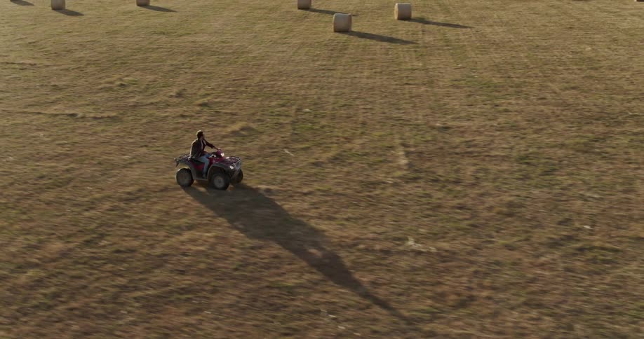 Man rides an all terrain vehicle on a field of hay bales at sunset