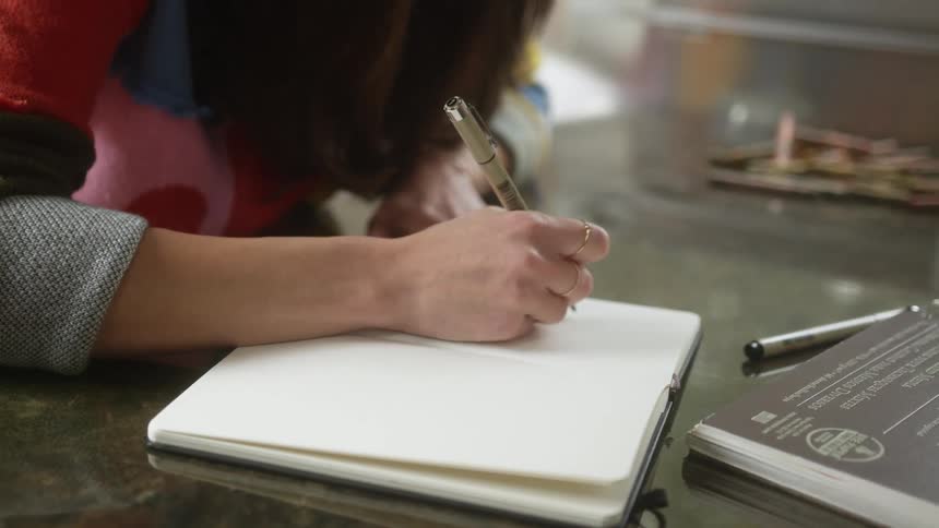 A woman sitting at a table drawing in a book with a pen