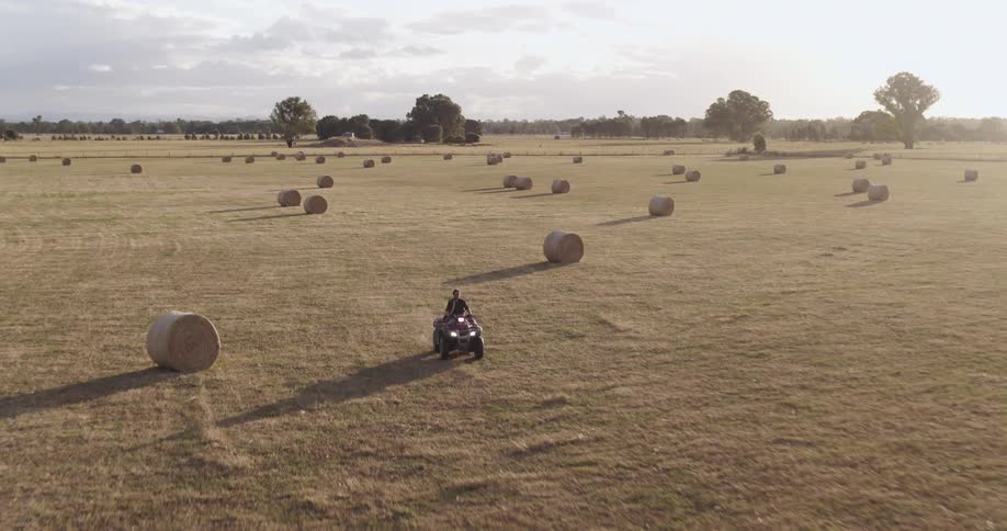 A man drives his tractor across farmland covered with hay bales