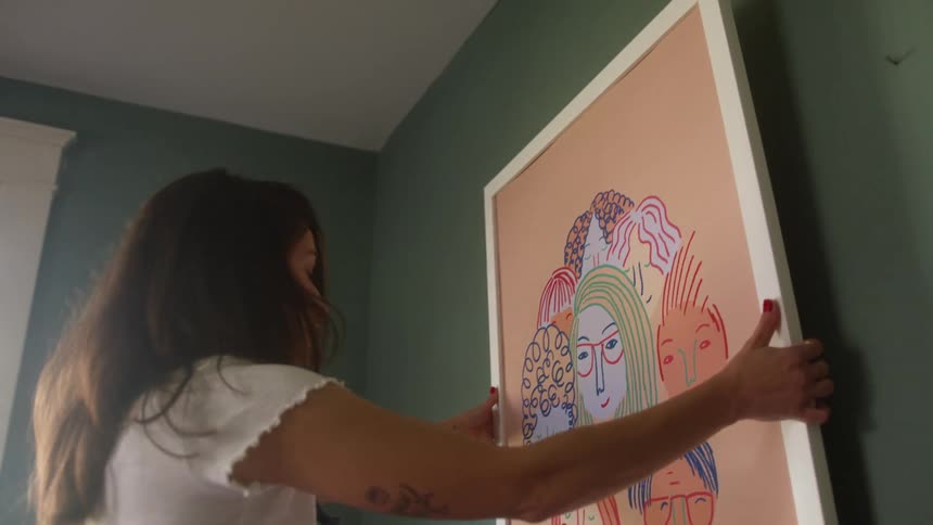 Woman hanging a picture frame on a nail in the wall at home