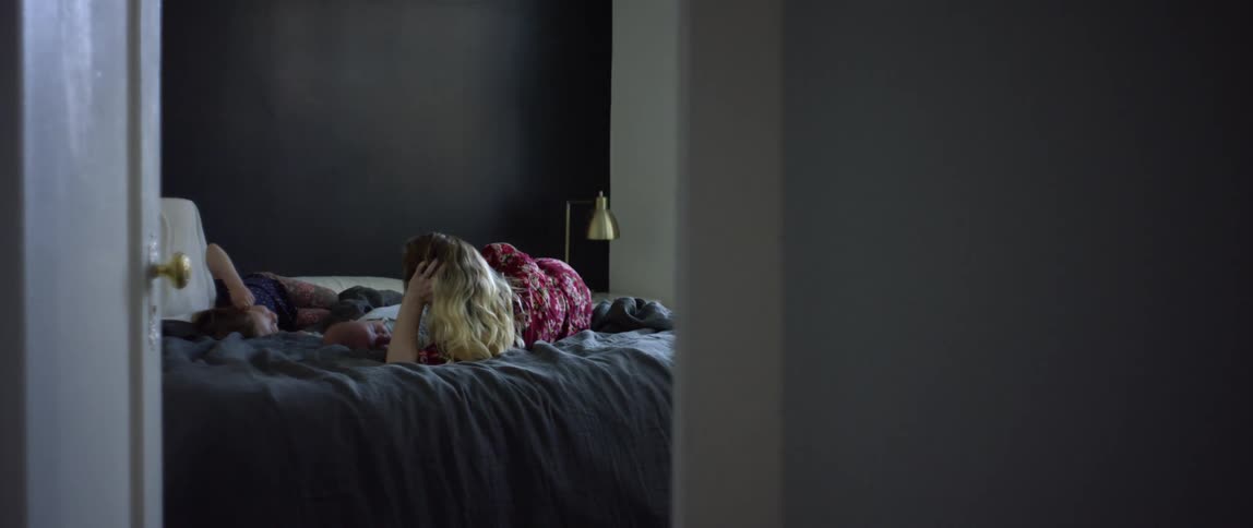 A woman chats with her young daughter as they lie in bed with her newborn