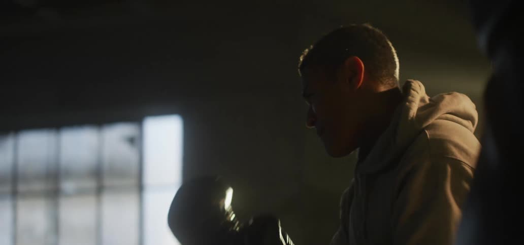 A boxer trains in a gym with his coach as bright sunlight shines through a window