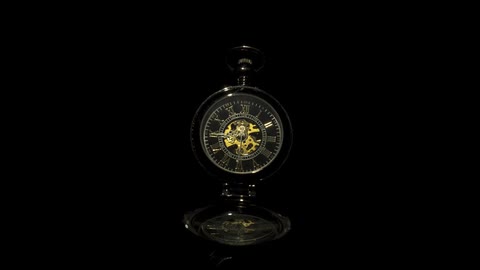 A gold clock with a stand is in darkness with the clock hands continually moving in a clockwise rotation