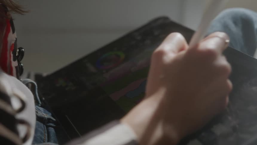 A woman is seated indoors and is using a writing utensil on a tablet