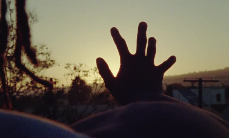 A person holds their hand up as the sun rises