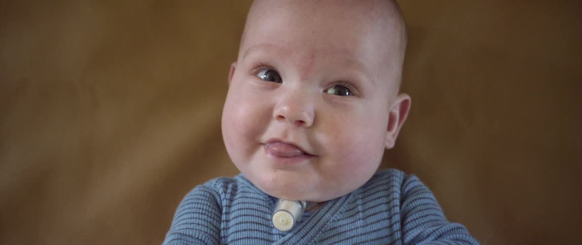 A baby in a blue top lies on his back smiling and moving hands