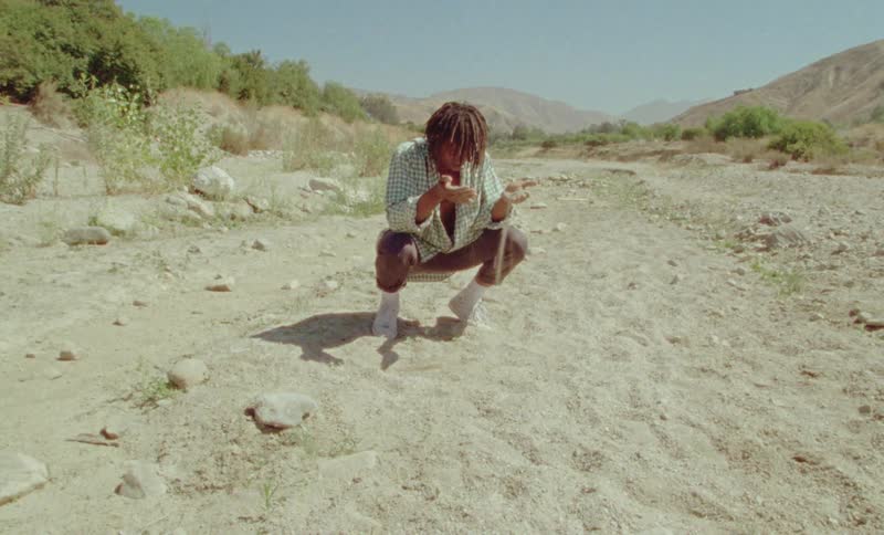 A teenage boy kneels down and watches as sand runs through his fingers