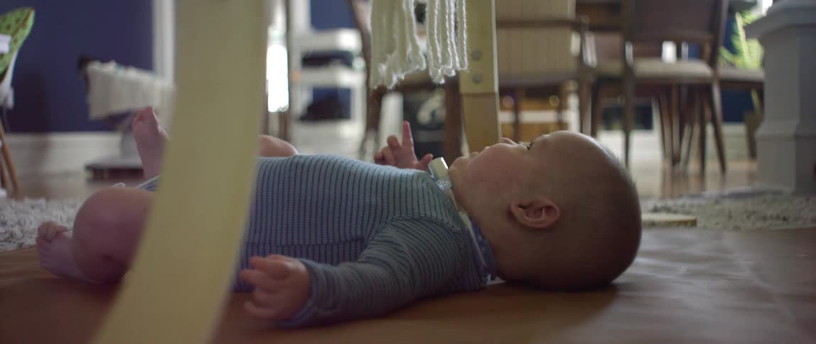A young baby lies on the floor under a toy and looks up at it