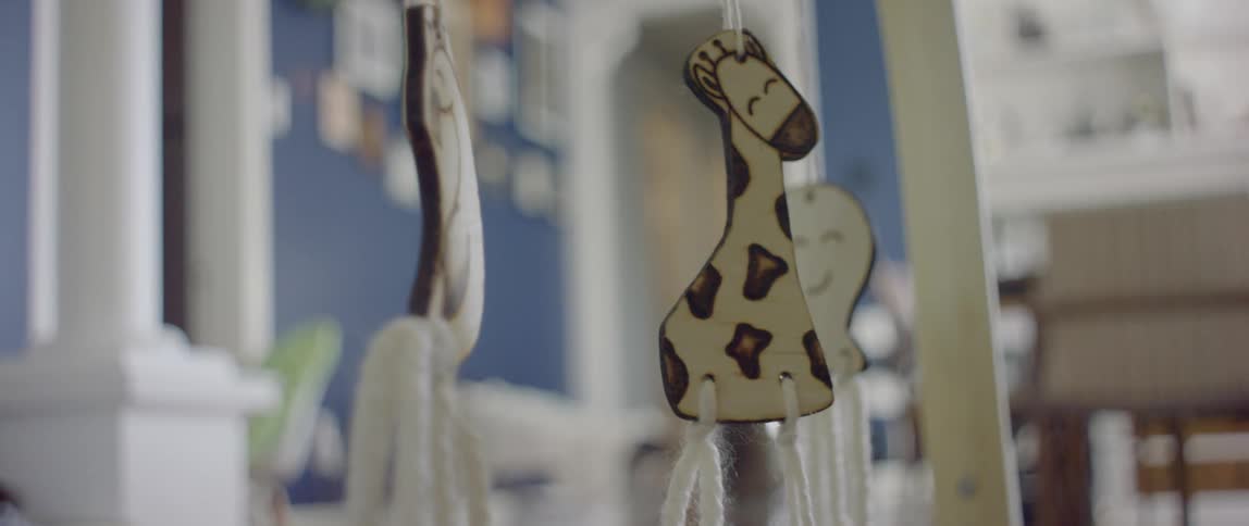 A baby lies on the floor touching a mobile with a giraffe