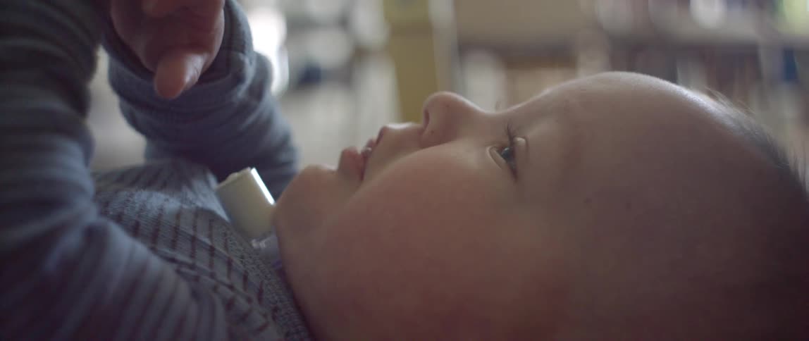 Baby with a tracheotomy tube laying on floor playing with his hands