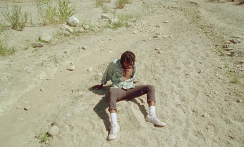 A man sitting on the ground with dirt rocks and plants
