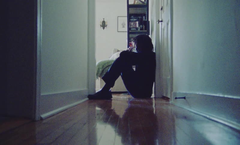 A man drinks from a glass while sitting in the hallway
